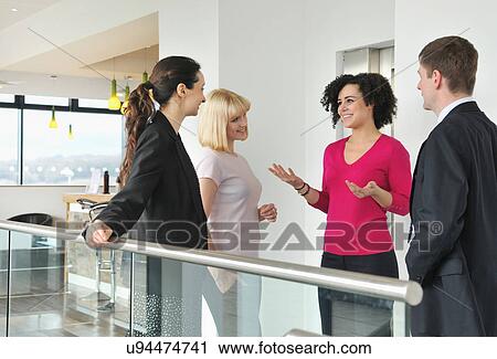 Stock Image - Four colleagues talking by railing in office building. Fotosearch