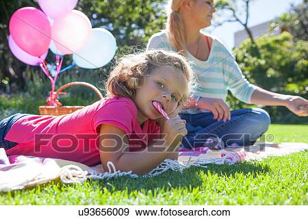 Stock Photo - Girl eating candy cane on blanket in garden. Fotosearch