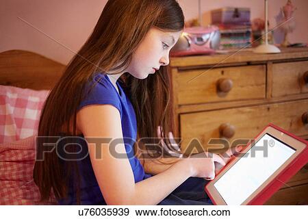 Stock Photo - Girl using digital tablet in bedroom. Fotosearch