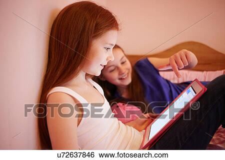 Stock Photograph - Girls using digital tablet together in bedroom. Fotosearch