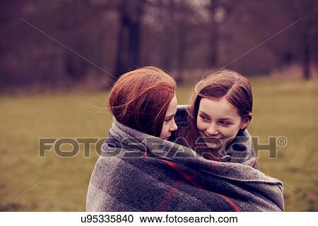 Stock Image - Girls wrapped in a blanket outdoors, smiling. Fotosearch