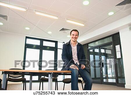 Male office worker sitting on table in office View Large Photo Image Stock Image - Male office worker sitting on table in office. Fotosearch