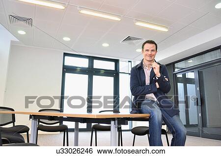 Stock Photograph - Male office worker sitting on table in office. Fotosearch