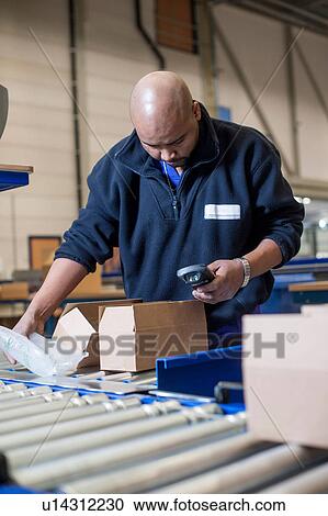 Stock Image - Male warehouse worker checking barcode scanner. Fotosearch