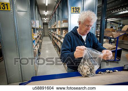 Picture - Male warehouse worker selecting item from conveyor belt. Fotosearch