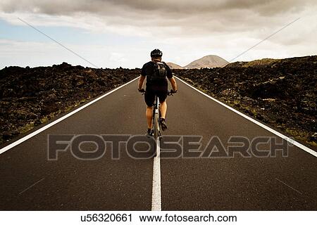 Stock Image - Man mountain biking on road, Lanzarote. Fotosearch