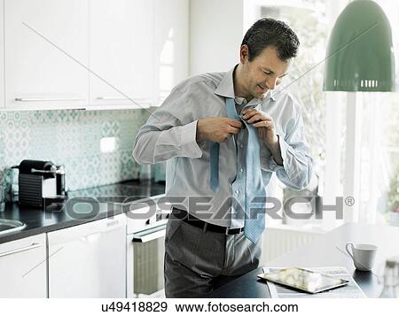 Stock Photo - Mature businessman getting ready and using tablet in kitchen. Fotosearch