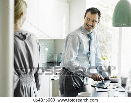 Stock Image - Mature businessman using tablet and smiling in kitchen. Fotosearch