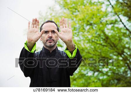 Picture - Mature man performing Tai Chi in countryside, front view. Fotosearch