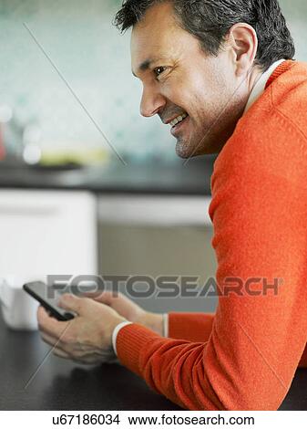 Mature man using cellphone in kitchen View Large Photo Image Picture - Mature man using cellphone in kitchen. Fotosearch
