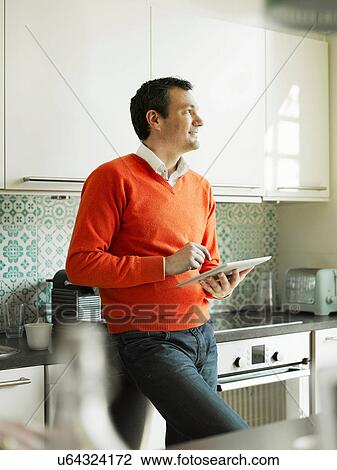 Stock Image - Mature man using tablet in kitchen. Fotosearch