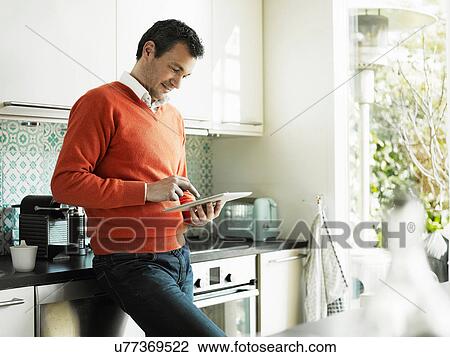 Stock Image - Mature man using tablet in kitchen. Fotosearch