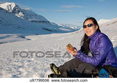 Stock Photograph - Mature woman enjoying sandwich in snow covered mountains, Skidadalur, Dalvik, Iceland. Fotosearch