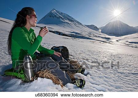 Picture - Mature woman sitting with a hot drink in snowy mountains, Skidadalur, Dalvik, Iceland. Fotosearch