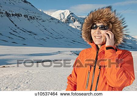 Picture - Mature woman using mobile phone in snow covered mountains, Skidadalur, Dalvik, Iceland. Fotosearch
