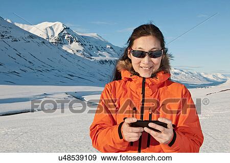 Stock Photo - Mature woman using smart phone in snow covered mountains, Skidadalur, Dalvik, Iceland. Fotosearch