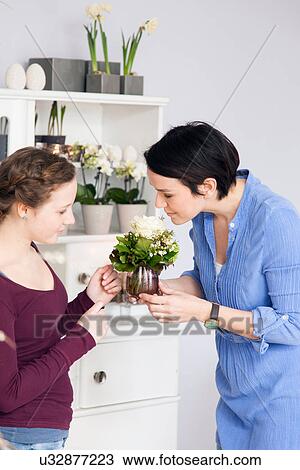 Stock Image - Mid adult woman and teenage girl smelling plants in florists. Fotosearch
