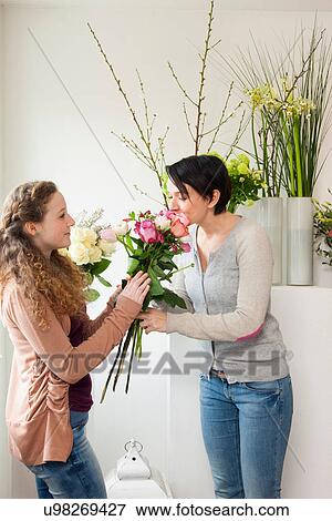Stock Photo - Mid adult woman and teenage girl smelling flowers in florists. Fotosearch