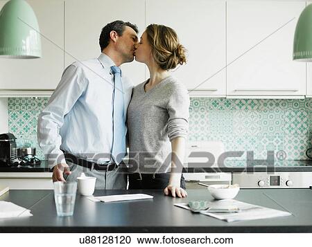 Stock Image - Mid adult woman kissing businessman in kitchen. Fotosearch