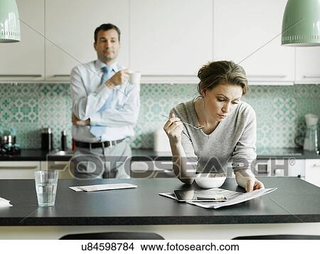Picture - Mid adult woman reading document over breakfast in kitchen. Fotosearch