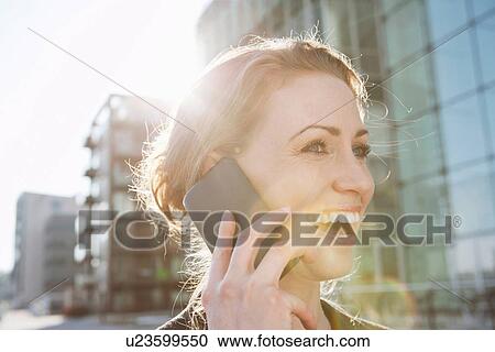 Mid adult woman using cellphone in sunlight outdoors View Large Photo Image Stock Image - Mid adult woman using cellphone in sunlight outdoors. Fotosearch