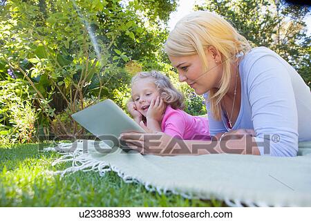 Mother and daughter lying on blanket in garden using digital tablet View Large Photo Image Stock Image - Mother and daughter lying on blanket in garden using digital tablet. Fotosearch