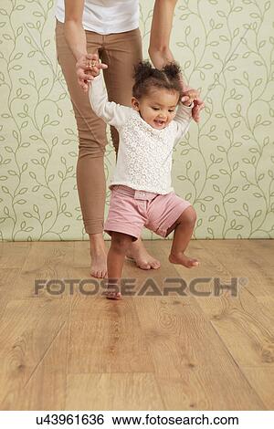 Mother holding baby girl taking first steps, low section View Large Photo Image Stock Photograph - Mother holding baby girl taking first steps, low section. Fotosearch