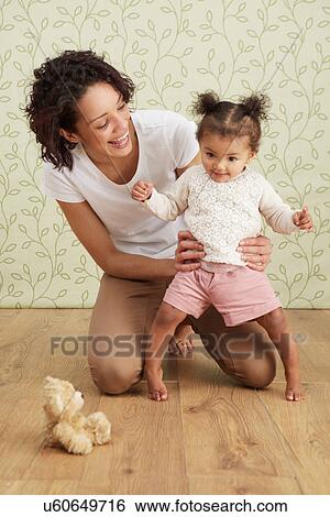 Stock Photograph - Mother holding baby girl taking first steps, smiling. Fotosearch