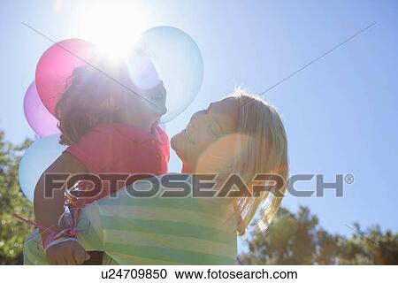 Mother hugging daughter in sunlight with basket of balloons View Large Photo Image Stock Image - Mother hugging daughter in sunlight with basket of balloons. Fotosearch
