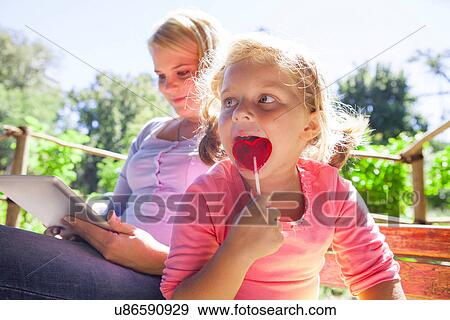 Mother using laptop, girl with lollipop View Large Photo Image Stock Photo - Mother using laptop, girl with lollipop. Fotosearch