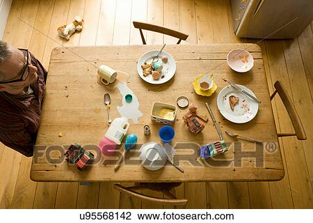 Stock Image - Overhead view of mature man sitting alone at messy breakfast table. Fotosearch