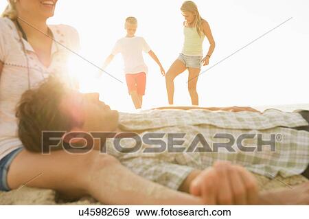 Parents relaxing on beach with children playing in background View Large Photo Image Stock Photo - Parents relaxing on beach with children playing in background. Fotosearch
