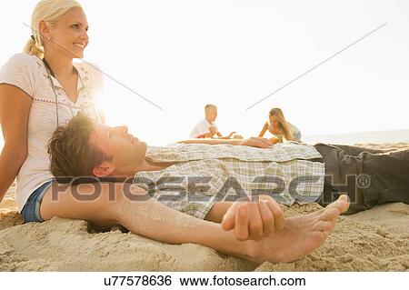 Stock Photograph - Parents relaxing on beach with children playing in background. Fotosearch