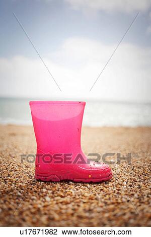 Stock Image - Pink rubber boot standing on sand. Fotosearch