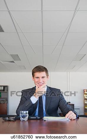 Stock Image - Portrait of businessman looking at camera with hand on chin. Fotosearch