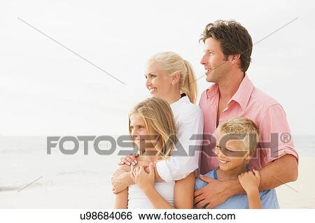 Stock Photograph - Portrait of family on beach with arms around each other. Fotosearch