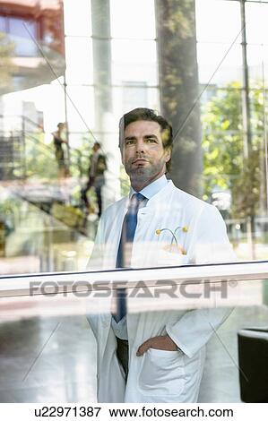 Stock Photo - Portrait of male doctor looking out of window. Fotosearch