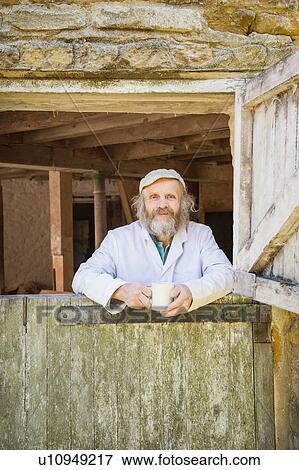 Stock Photo - Portrait of man looking through windmill door holding mug. Fotosearch