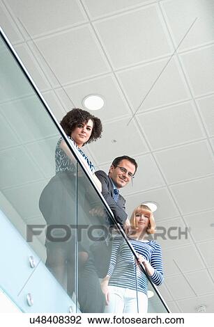 Stock Image - Portrait of three colleagues leaning on railing, low angle. Fotosearch