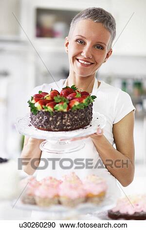 Stock Image - Portrait of woman holding cake with strawberries. Fotosearch