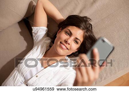 Stock Photo - Portrait of woman lying on sofa holding cell phone. Fotosearch