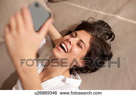 Portrait of woman lying on sofa holding cell phone View Large Photo Image Stock Photograph - Portrait of woman lying on sofa holding cell phone. Fotosearch
