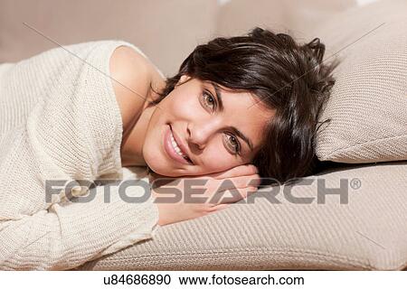 Stock Image - Portrait of woman lying on sofa looking at camera. Fotosearch