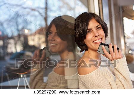 Stock Image - Portrait of woman outside cafe holding cell phone. Fotosearch