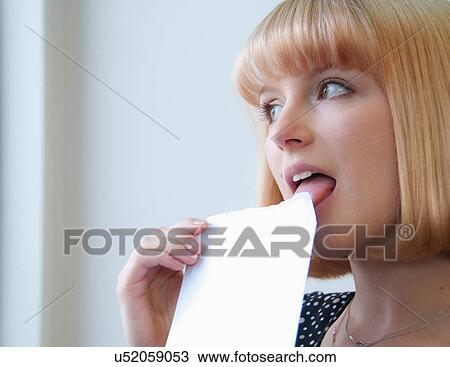 Stock Image - Portrait of woman with blonde bob licking envelope. Fotosearch