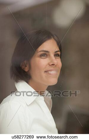 Stock Photo - Portrait of young female looking through window. Fotosearch