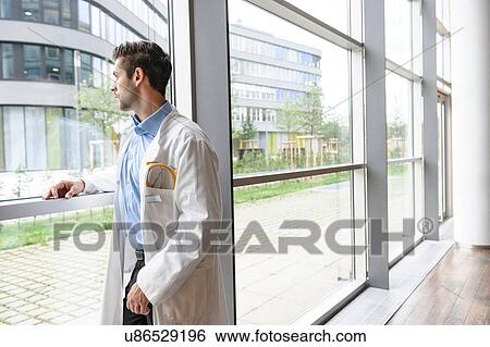 Portrait of young male doctor looking out of window View Large Photo Image Stock Photograph - Portrait of young male doctor looking out of window. Fotosearch