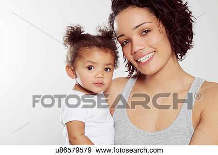 Stock Photo - Portrait of young woman holding baby daughter in studio. Fotosearch