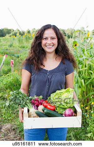 Portrait of young woman holding box of fresh vegetables in allotment View Large Photo Image Stock Image - Portrait of young woman holding box of fresh vegetables in allotment. Fotosearch