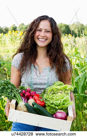 Portrait of young woman holding box of fresh vegetables in allotment View Large Photo Image Stock Photo - Portrait of young woman holding box of fresh vegetables in allotment. Fotosearch